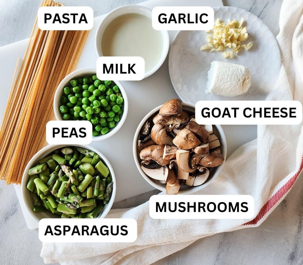 veggie pasta recipe ingredients on white plate and in white bowls: pasta, garlic, milk, peas, asparagus, goat cheese, mushrooms
