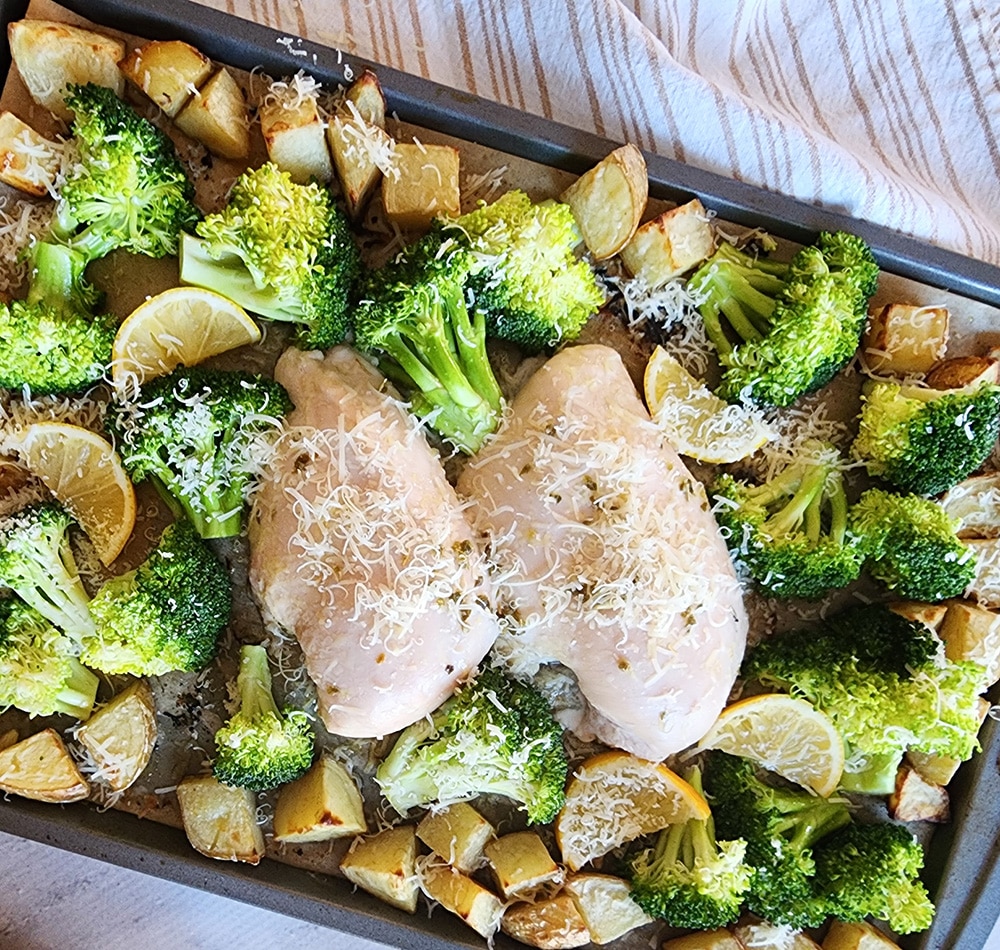 a picture of broccoli, chicken and potatoes on a sheet pan with cheese on top ready for the oven