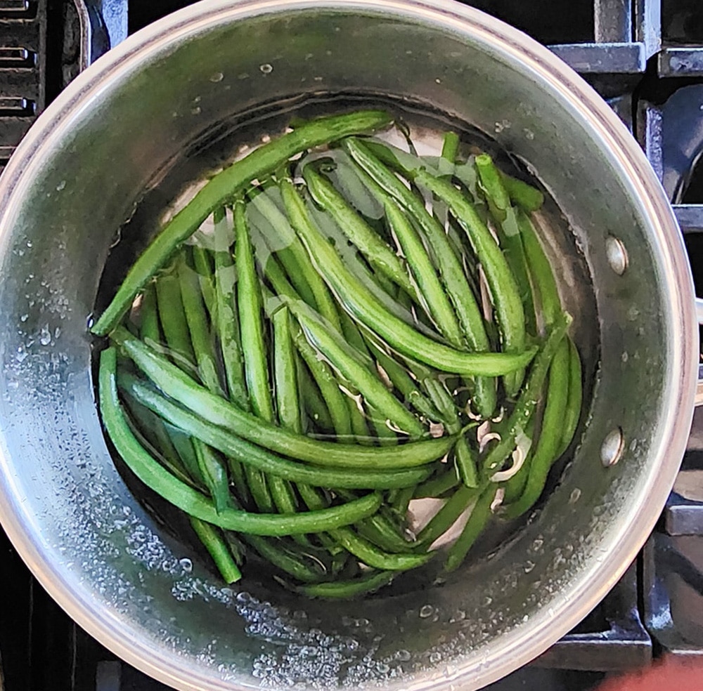 Step one blanch the beans - A picture of green beans in a sauce pan in water