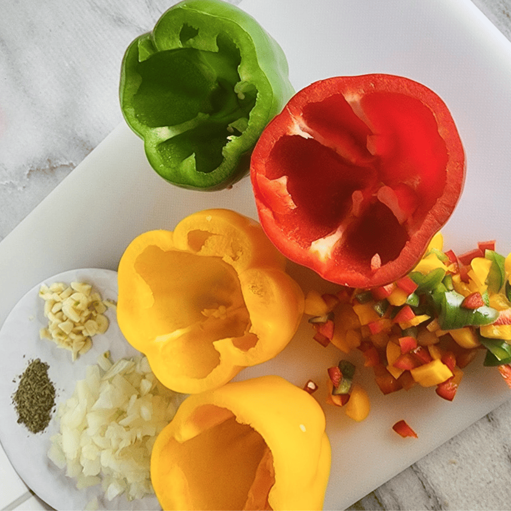 hollowed out bell peppers on a cutting board with chopped onions and garlic on the side.