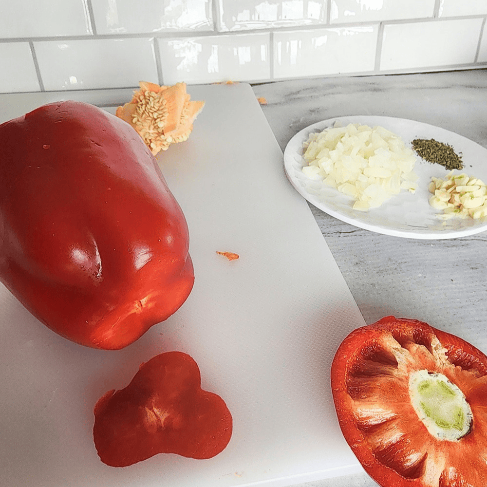 a red bell pepper on a cutting board with the top sliced off as well as a slice of the bottom 