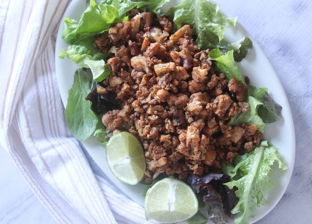 an overhead view of vegetarian taco meat on a white platter with lettuce and lime wedges