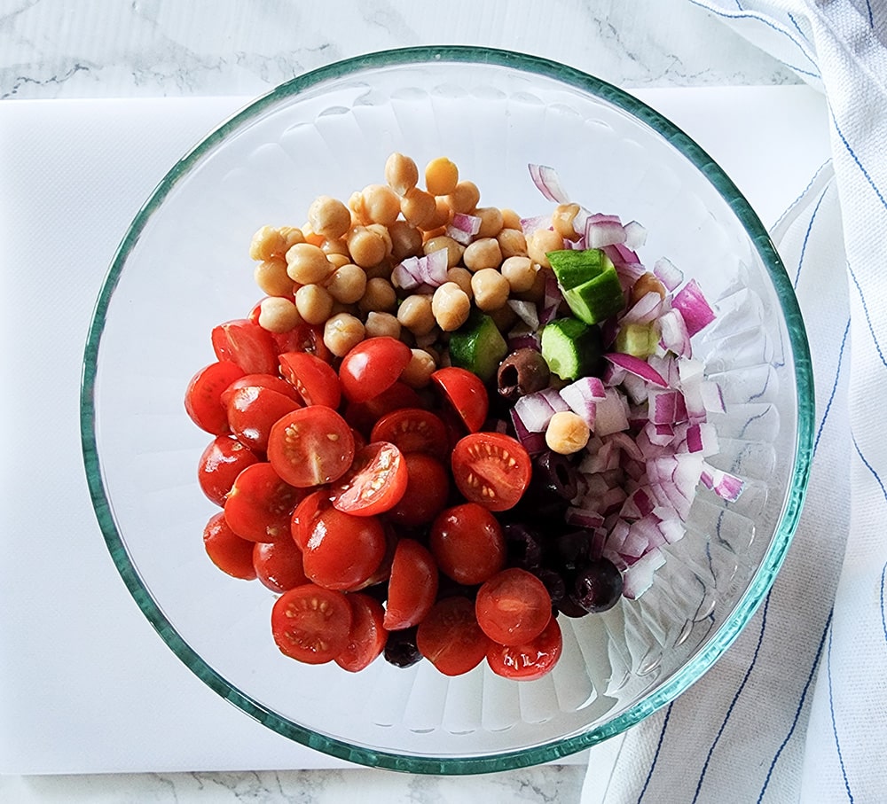 a picture of tomatoes, onions, chickpeas and cucumbers in a bowl