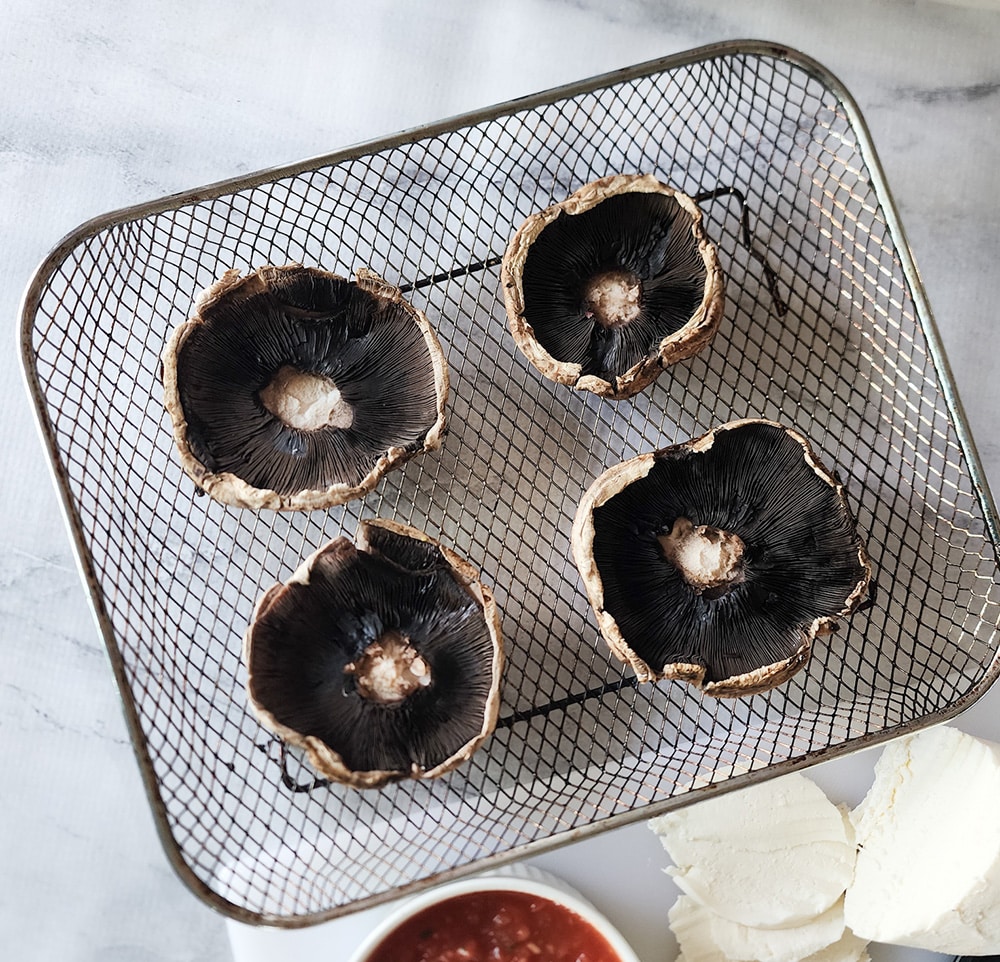 This image shows a photo of 4 portobello mushroom caps gill side up on an air fryer tray 