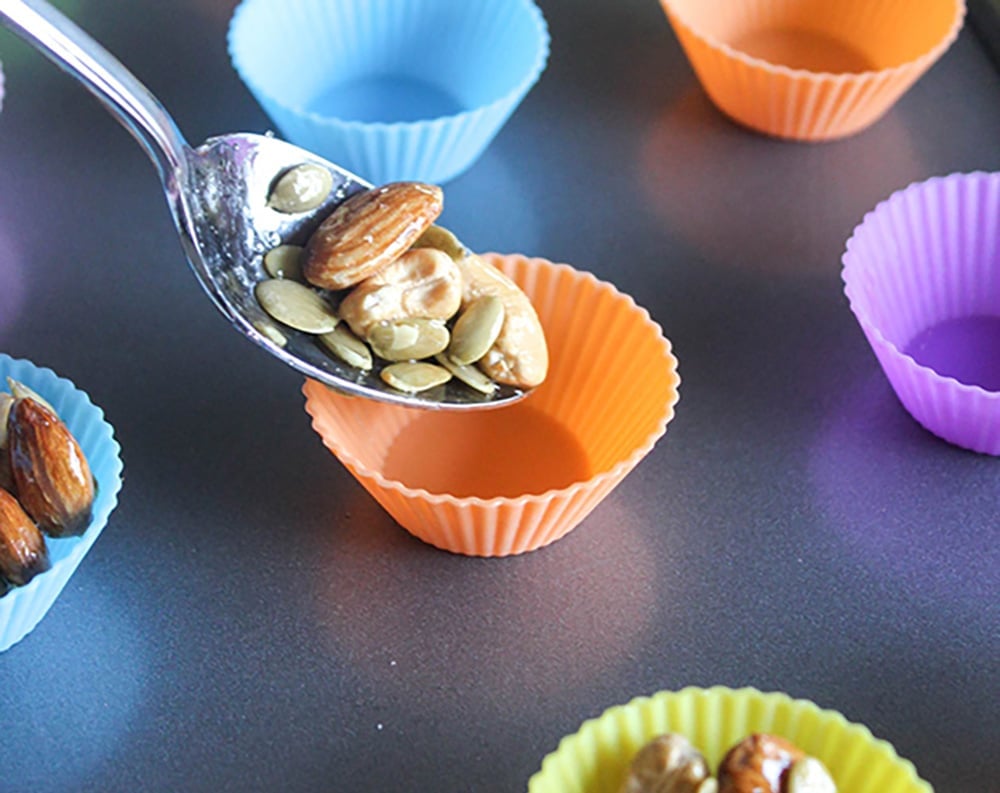 A picture of a spoon dropping the cashew cluster mixture into an orange silicone cup