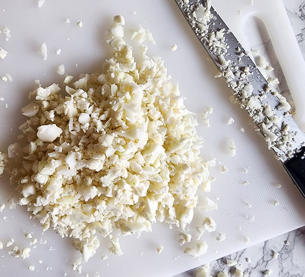 a picture of riced cauliflower on a cutting board with a knife on the side.