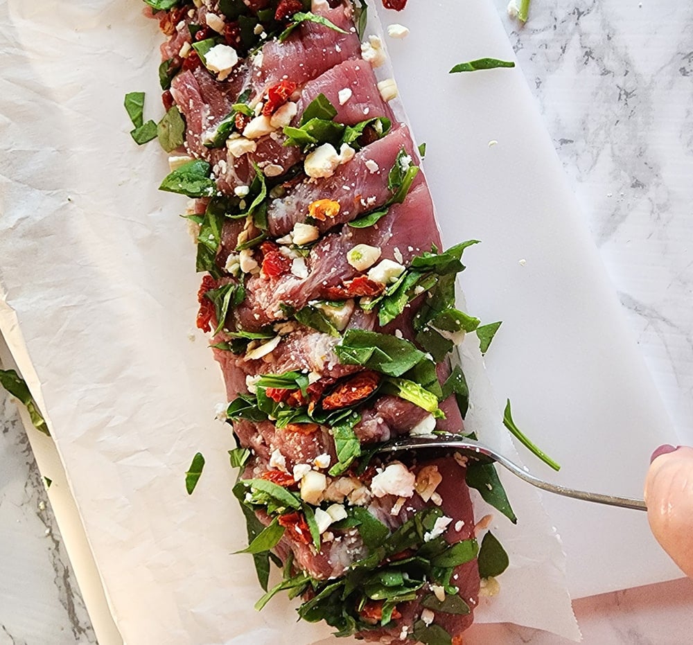 a picture of a  the stuffing being added to the pork tenderloin with a spoon