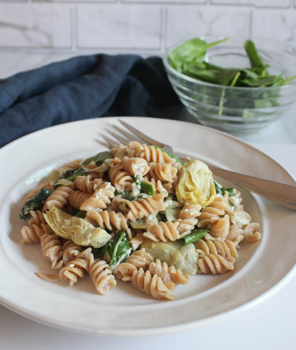 a picture of spinach artichoke pasta on a white plate with a fork