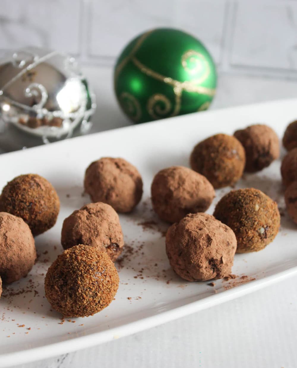 a picture of rolled sugar plums on a white platter with christmas ornamants in the background
