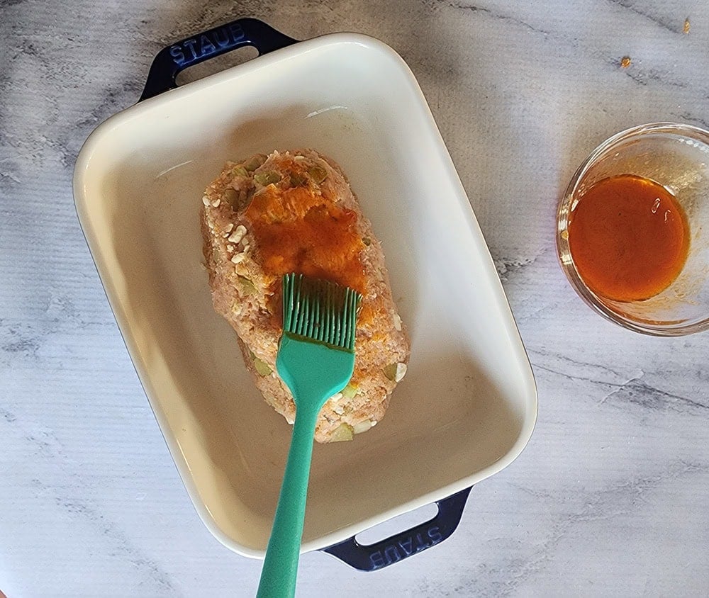 a picture of a formed meatloaf with a brush covering the meatloaf with sauce