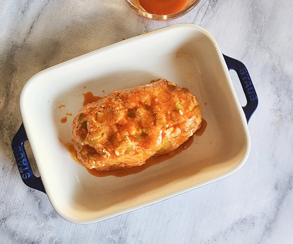 a picture of a chicken meatloaf covered with sauce ready for the oven
