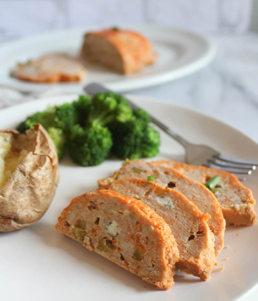 A picture of buffalo chicken meatloaf on a plate with broccoli, potatoe and a fork