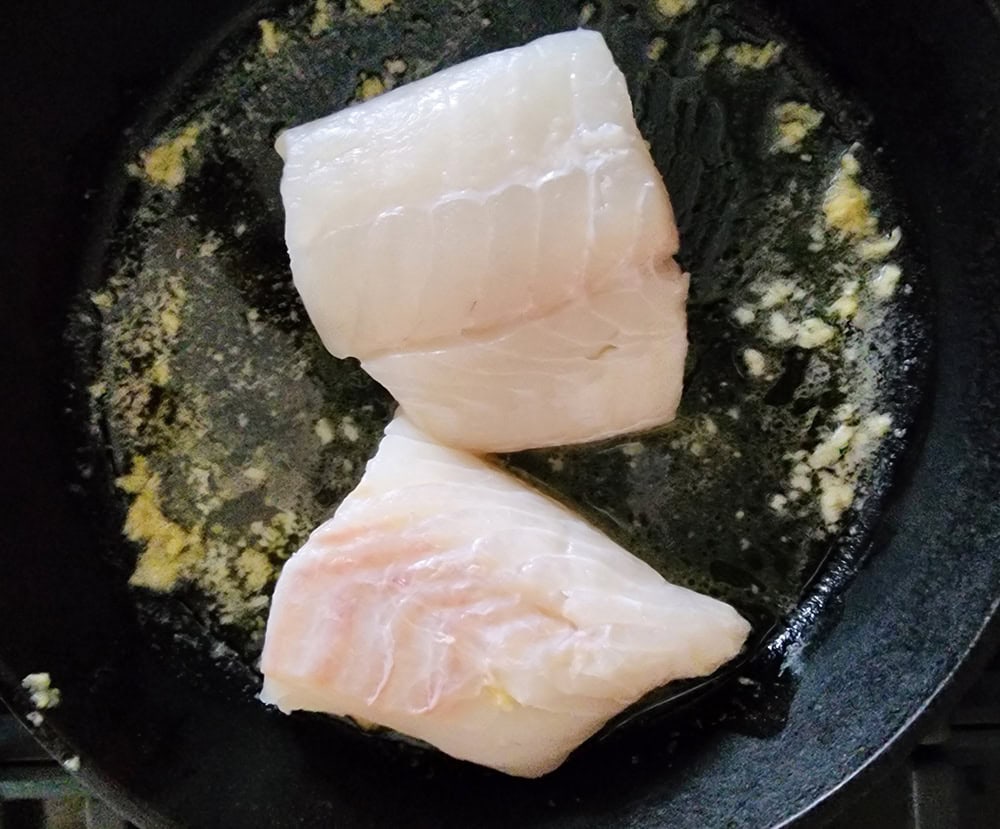 a picture of two fish filets in a pan of garlic butter