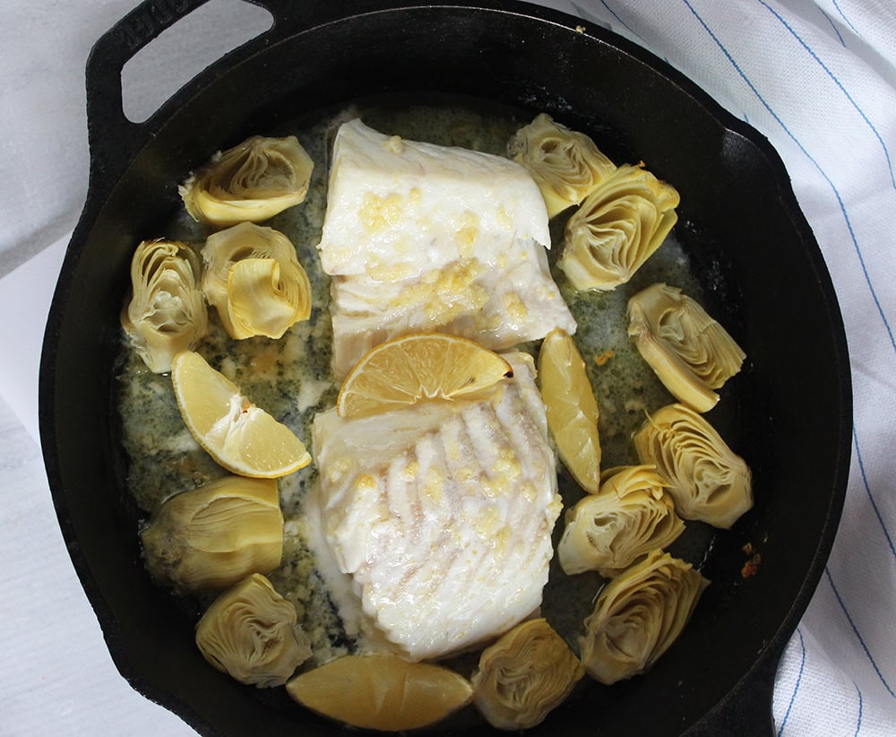 a picture of the dish out of the oven two fish filets with lemon slices and artichoke hearts