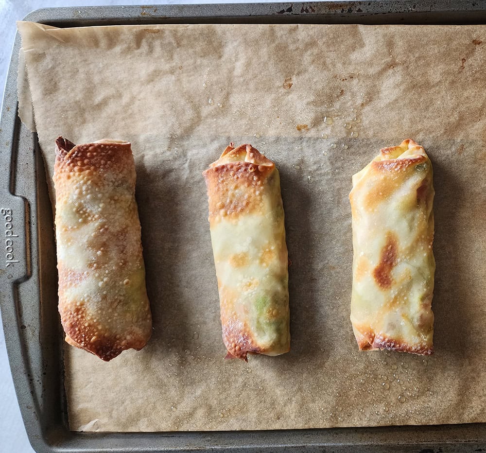 a picture of crispy baked egg rolls on a parchment line baking sheet