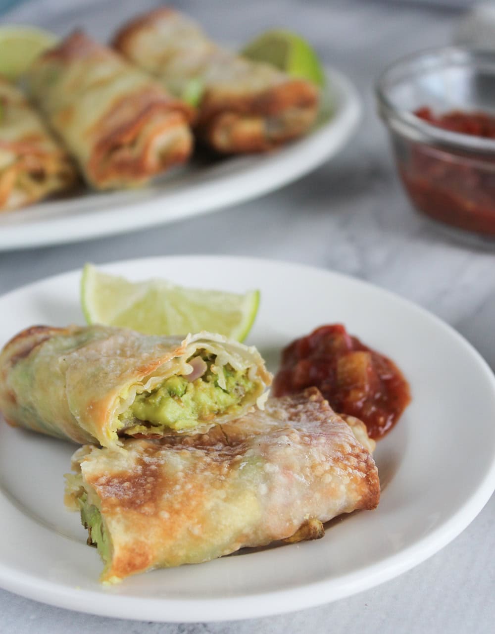 crispy baked avocado egg rolls on a serving plate with lime wedges and salsa.
