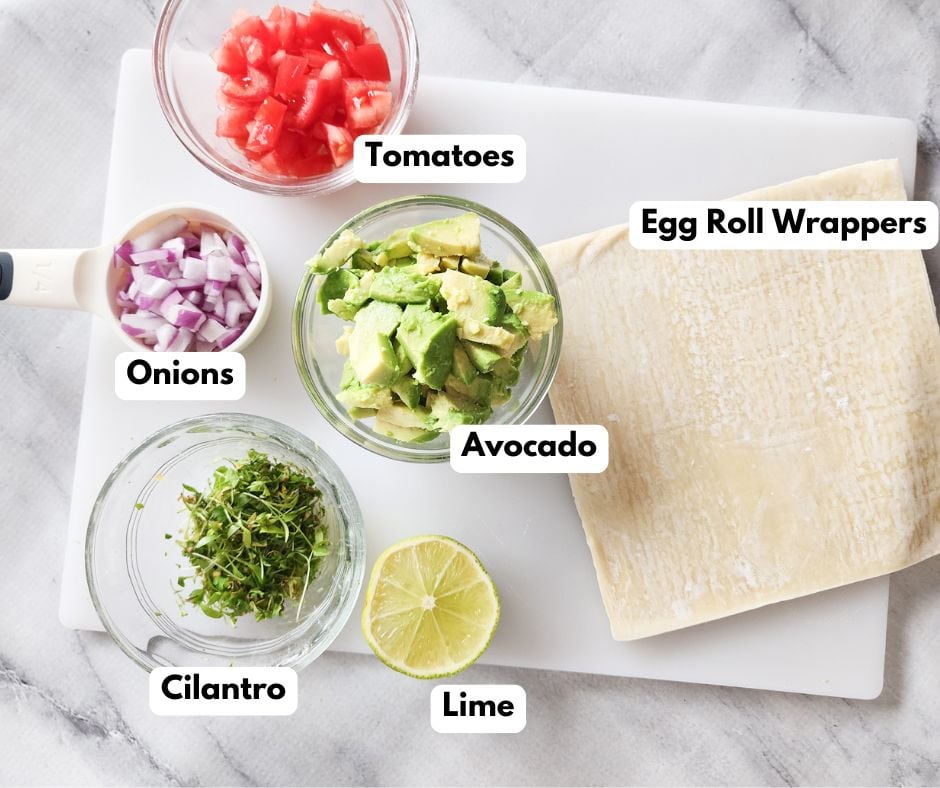 the ingredients needed to make baked avocado eggrolls in separate bowls: cilantro, onions, tomatoes, avocado, lime, egg roll wraps