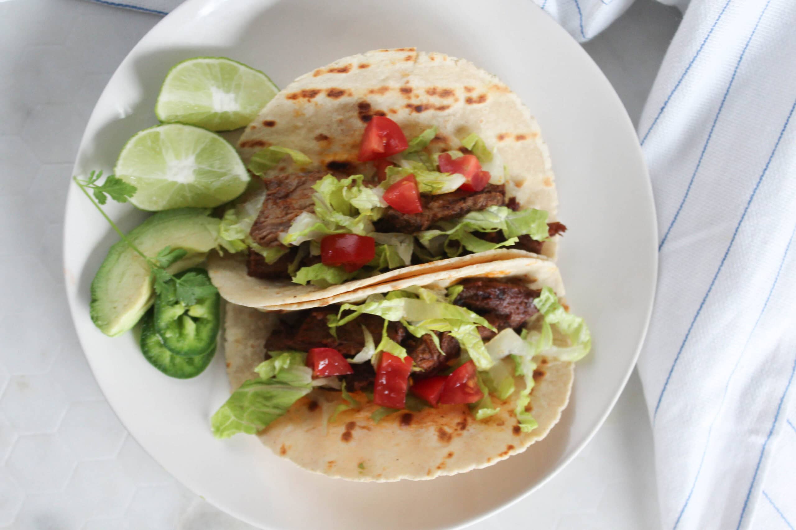 an overhead view of two shredded beef tacos on a plate with shredded lettuce and lime wedges