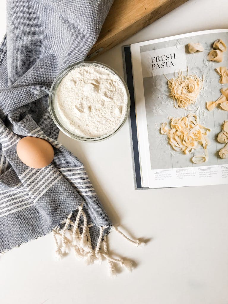 Top view of fresh pasta ingredients with cookbook guidance, ready for culinary creation.