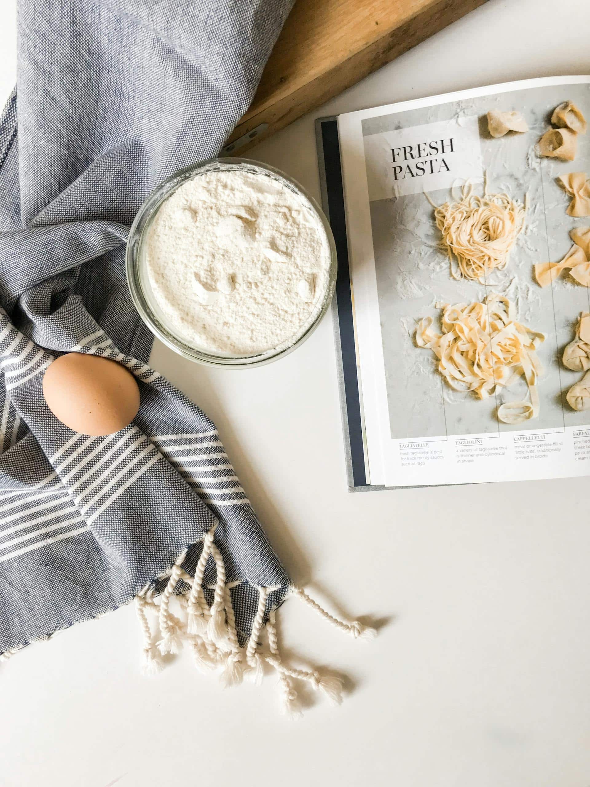 Top view of fresh pasta ingredients with cookbook guidance, ready for culinary creation.