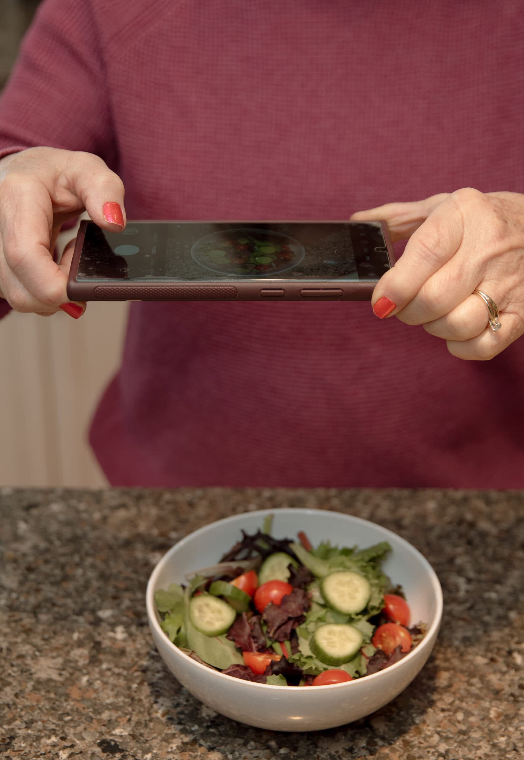 a picture of anne's hands holding a phone over a salad shooting a picture
