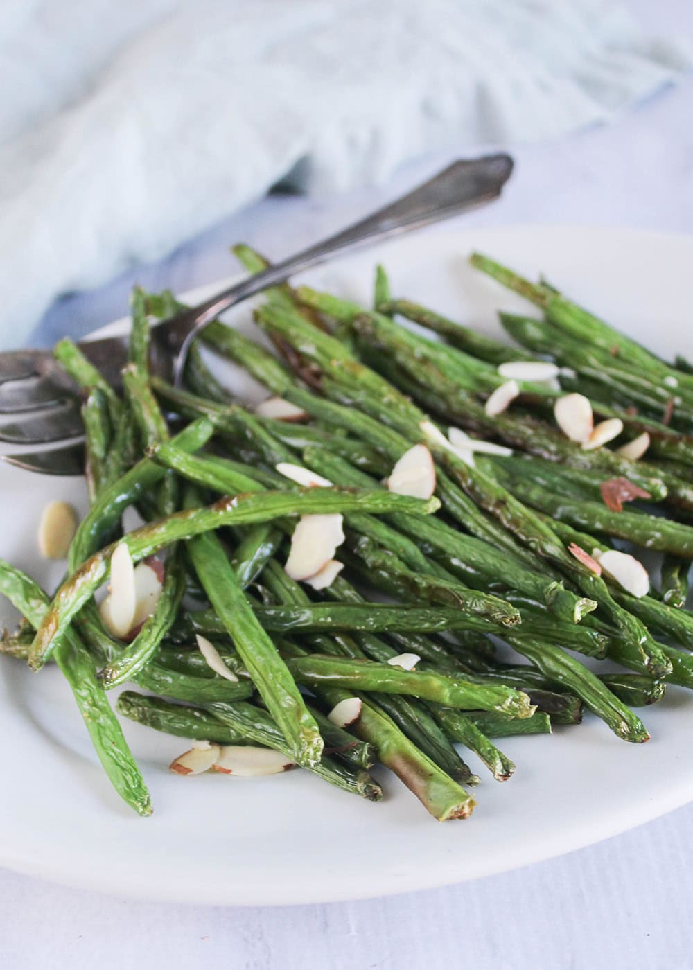Air fried green beans on a white platter with a serving fork