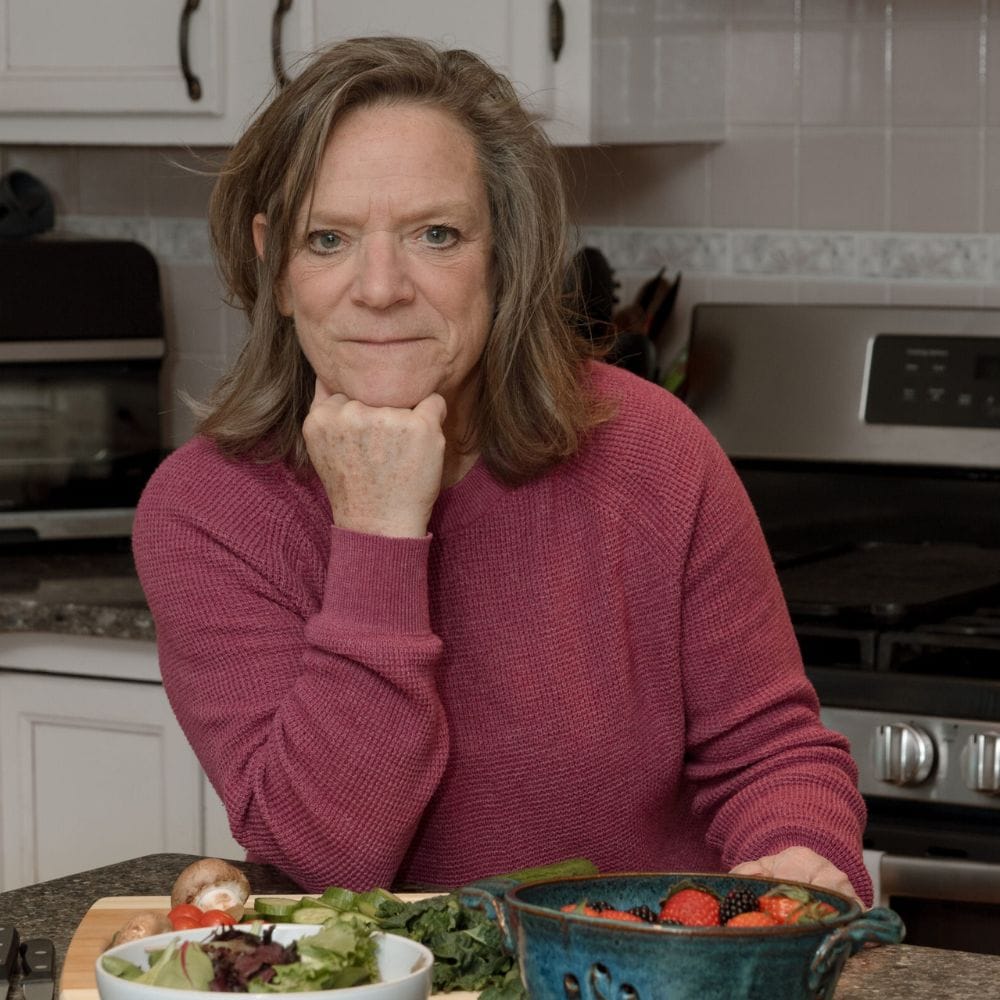 A picture of the author, Anne at her kitchen counter with bowls of fruit and veggies