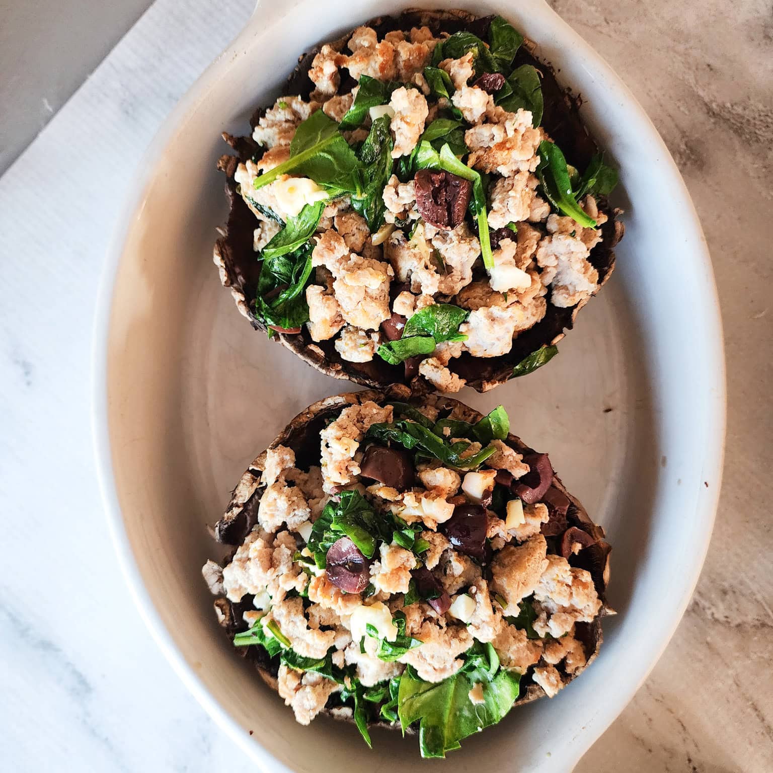 Image 3 (Stuffed Mushrooms Pre-Bake, Top View): Two large portobello mushroom caps filled with an uncooked mixture of ground turkey, spinach, olives, and cheese, arranged side by side in an oval baking