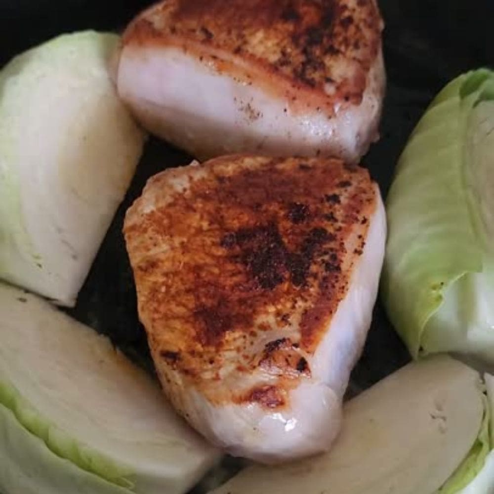 two boneless pork chops cookng in skillet with added cabbage wedges.