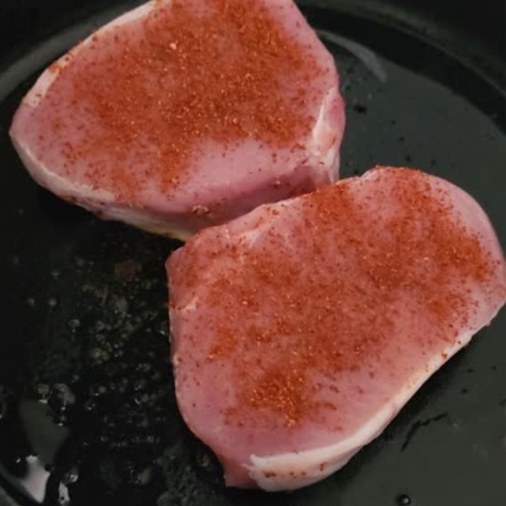 two seasoned  boneless pork chops cooking in a cast iron skillet