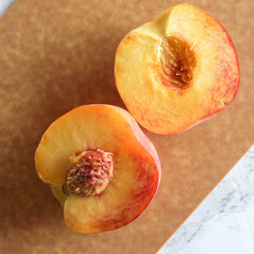 a picture showing a peach cut in half on a cutting board with a pit in on half of the peach