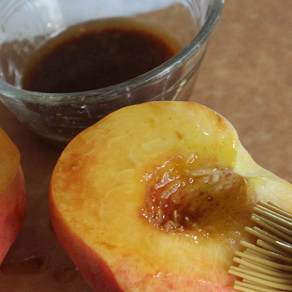 a picture of marinade being brushed onto a peach half with a silicone pastry brushl