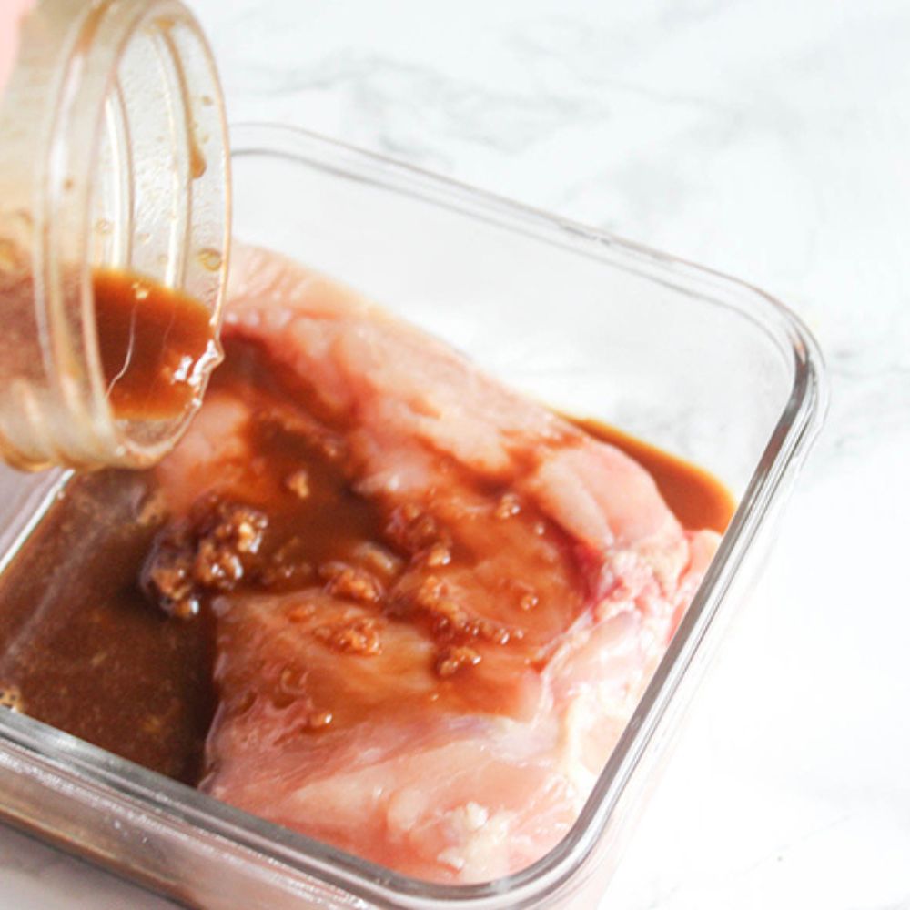 a picture of boneless chicken breasts in a glass bowl with balsamic marinade pouring in