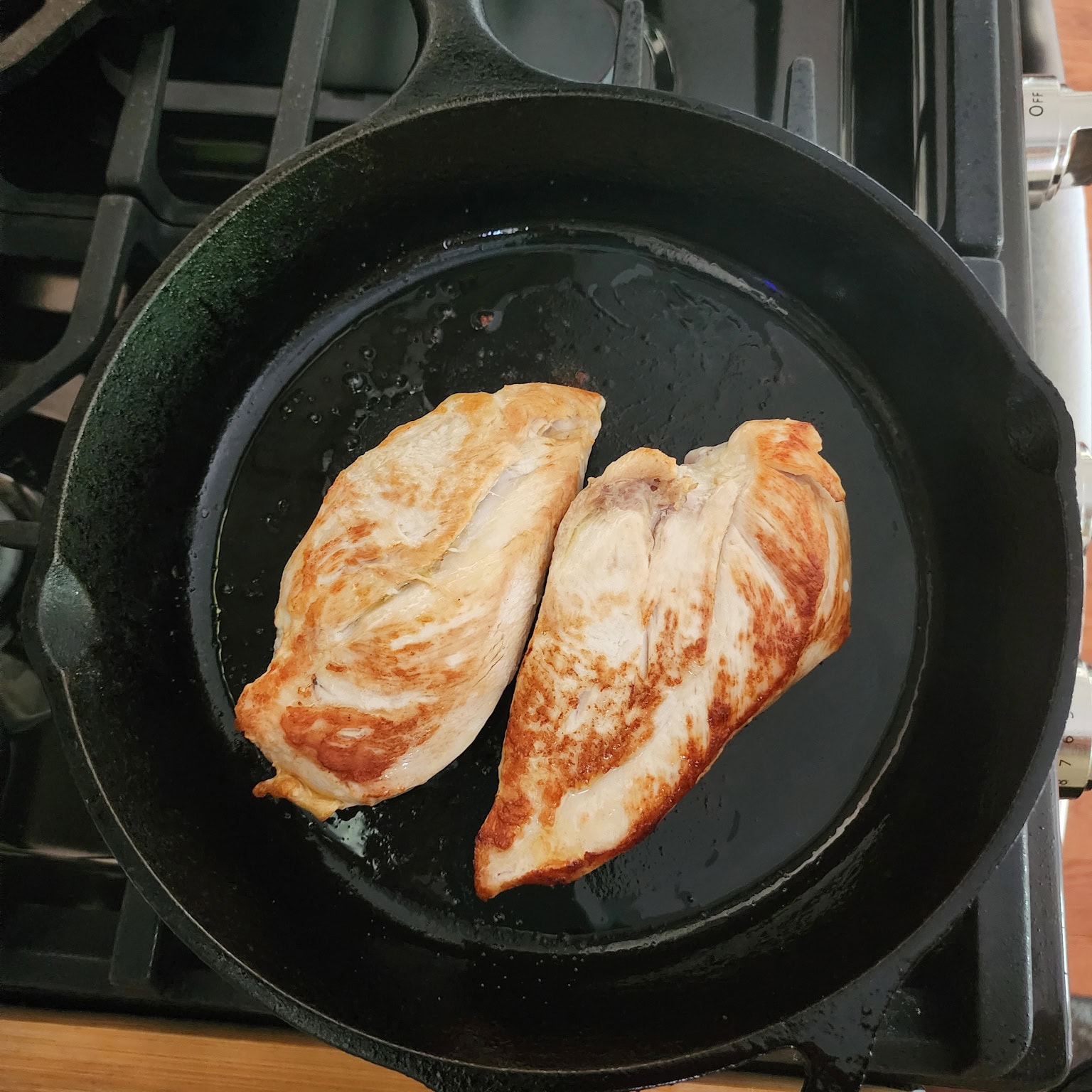 two boneless chicken breasts cooking in a skillet 