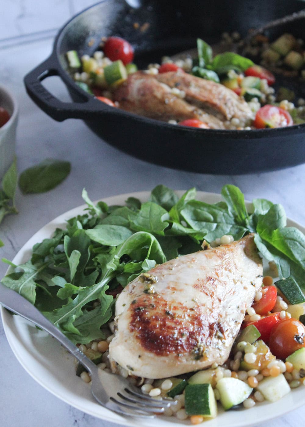 a chicken breast on a plate sitting on top of couscous and vegetables with a salad on the side of the plate