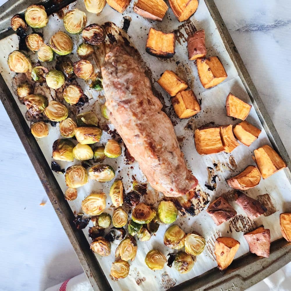 sheet pan pork tenderloin cooked on a sheet pan with sweet potatoes and brussels sprouts
