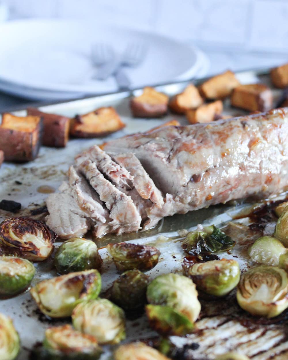 A picture of sliced pork tenderloin on a sheet pan with cooked vegetables on a sheet pan