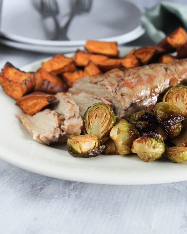 a picture of pork tenderloin sliced on a platter with sweet potatoes and brussels sprouts