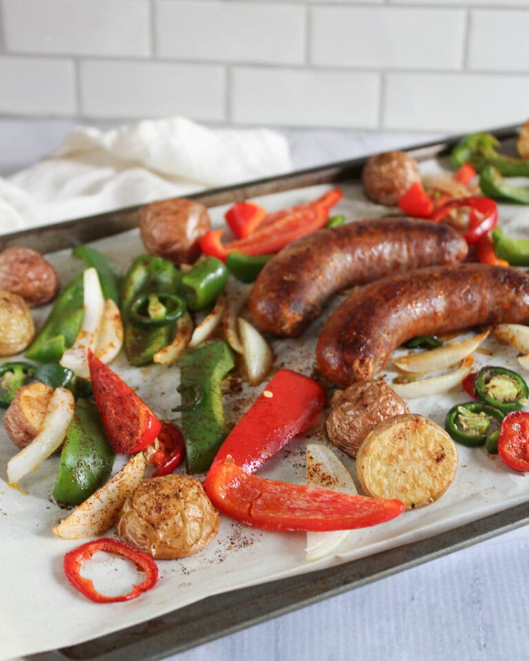 two sausages on a sheet pan with potatoes, peppers and onions surrounding them