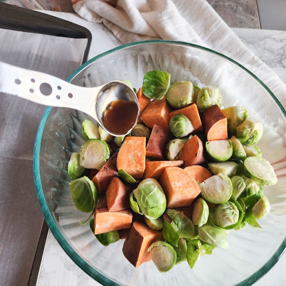 A picture of the veggies in a glass bowl with sauce pouring in