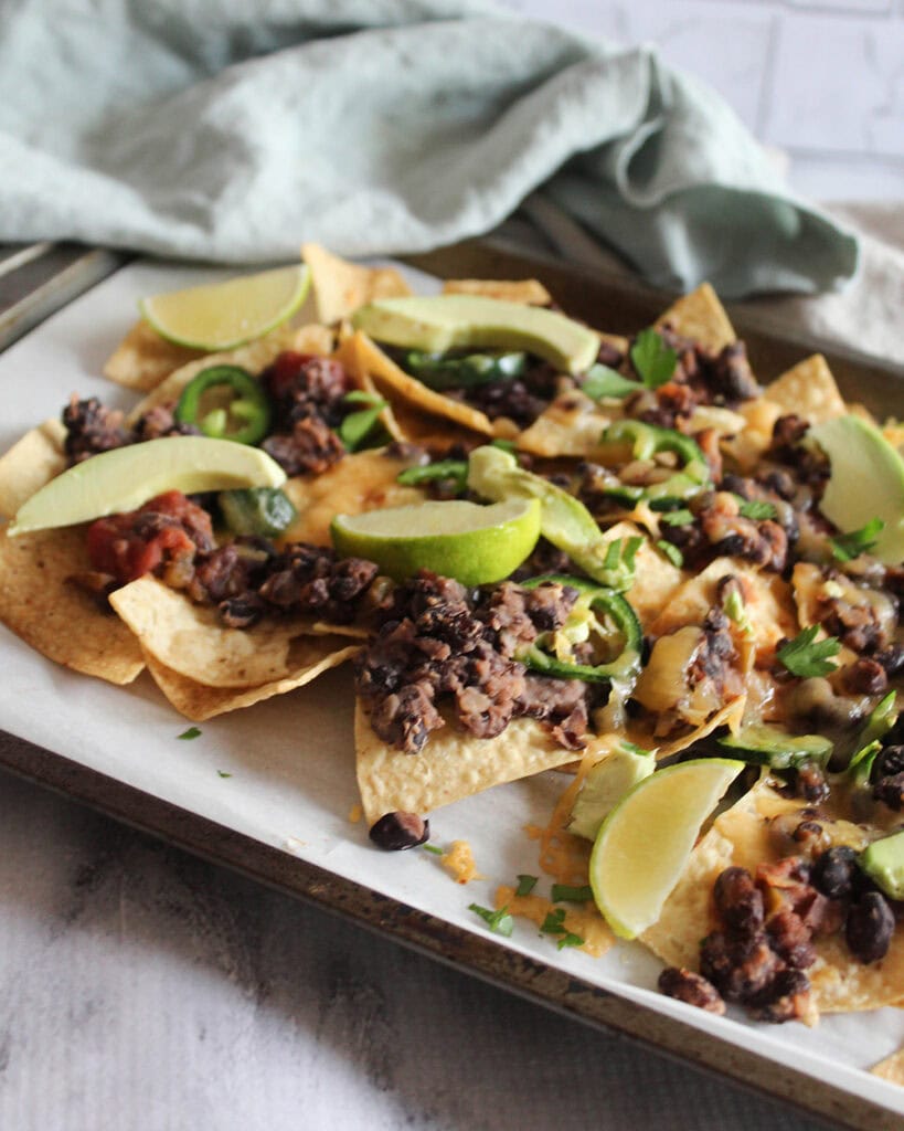 a picture of cooked sheet pan nachos with jalapeno peppers, avocado and lime slices on top
