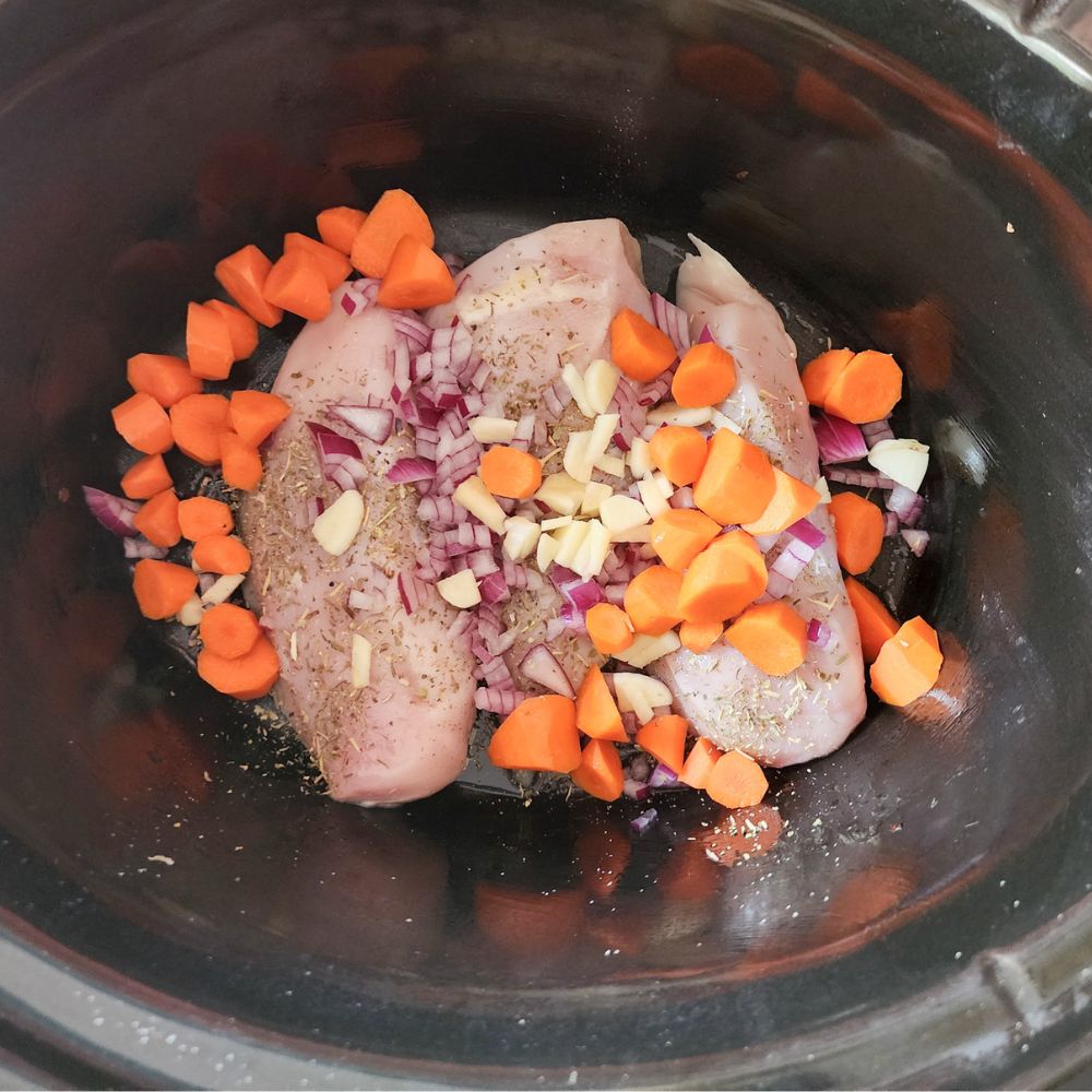 Tuscan chicken step 2, two chicken breasts with carrots and onions on top in a slow cooker