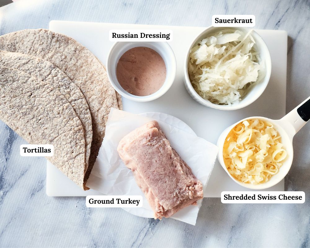 An overhead view of the ingredients needed to make turkey wraps: tortillas, ground turkey, cheese, sauerkraut and russian dressing