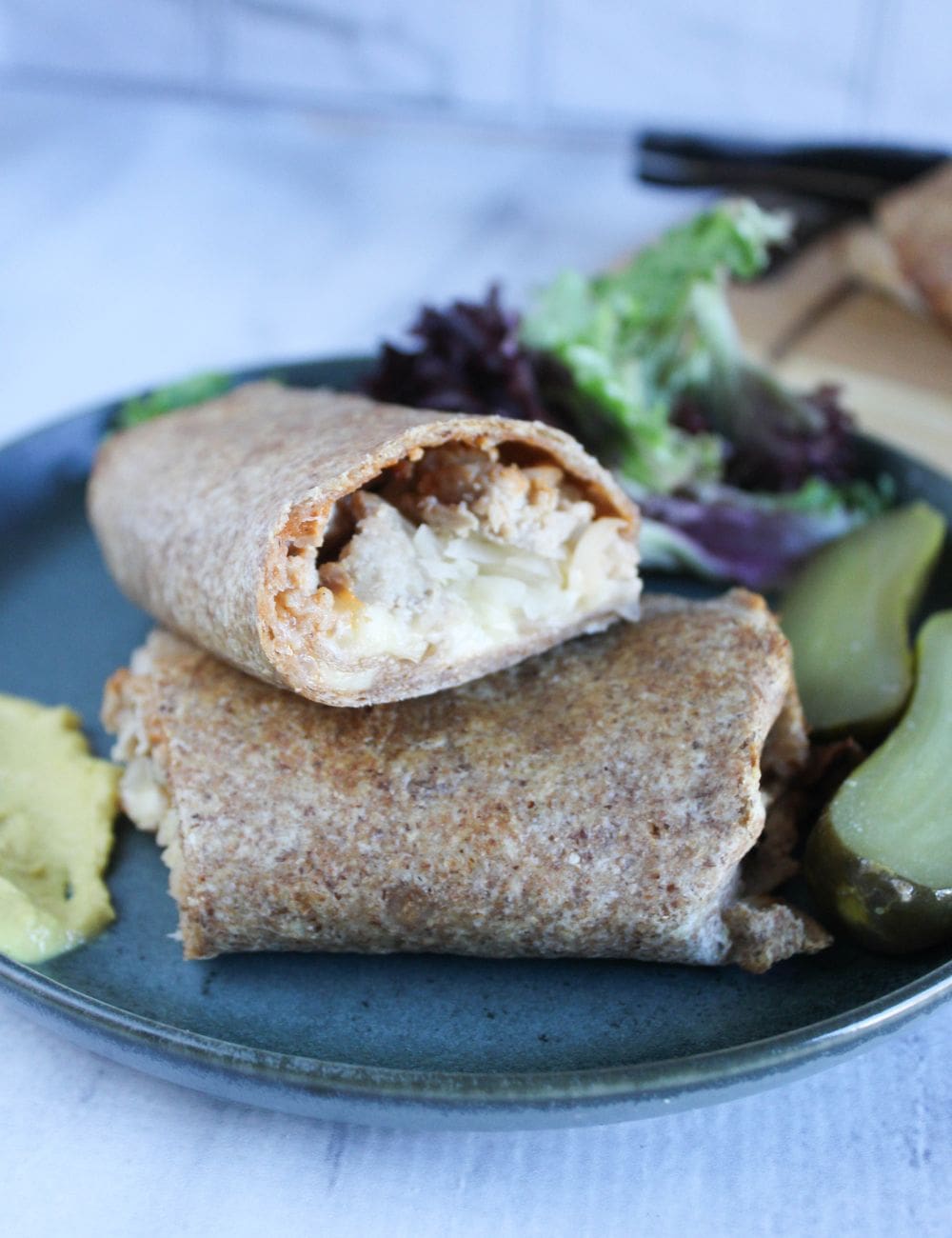 a picture of finished turkey wraps on a plate stacked on top of each other with pickles and mustard on the side