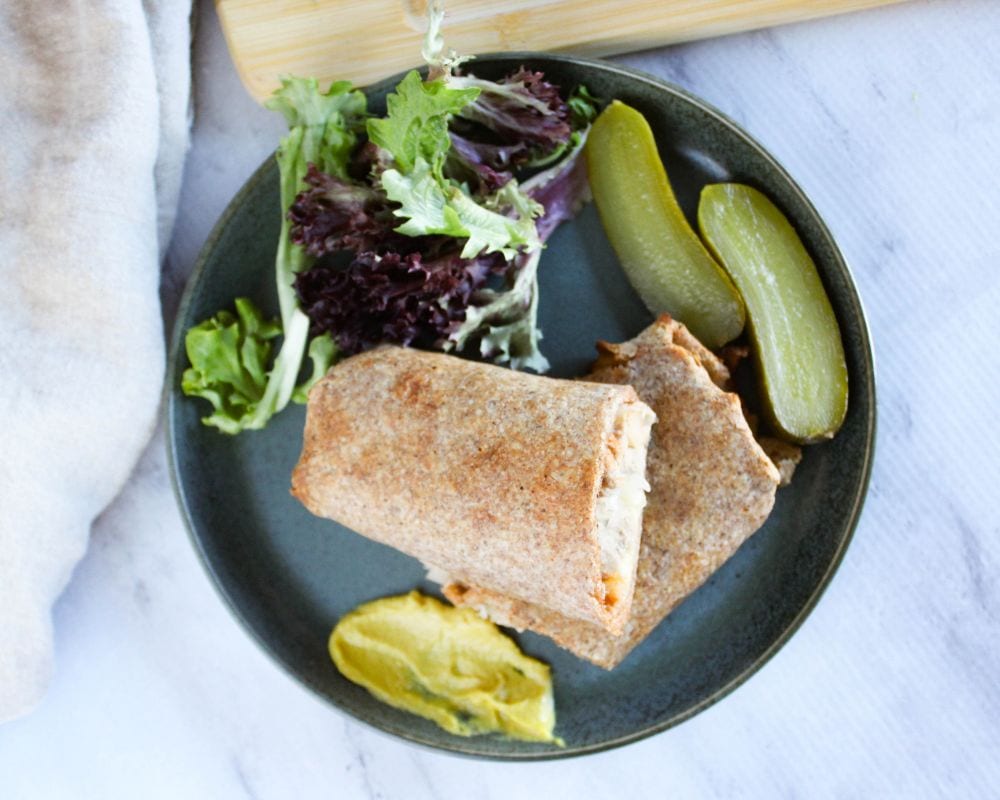 an overhead shotof turkey wraps on a blue plate with pickles, lettuce and mustard