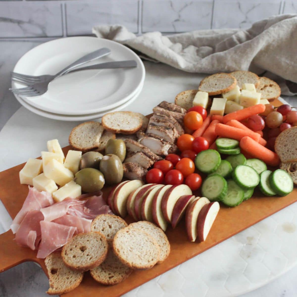a picture of a healthy charcuterie board with apples, sliced vegetables, grapes, cheese and sliced grilled chicken