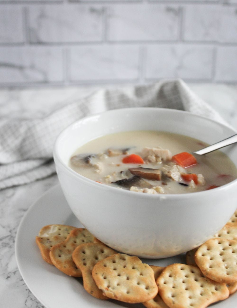 creamy turkey soup in a white bowl with a plate of crackers surrounding it 