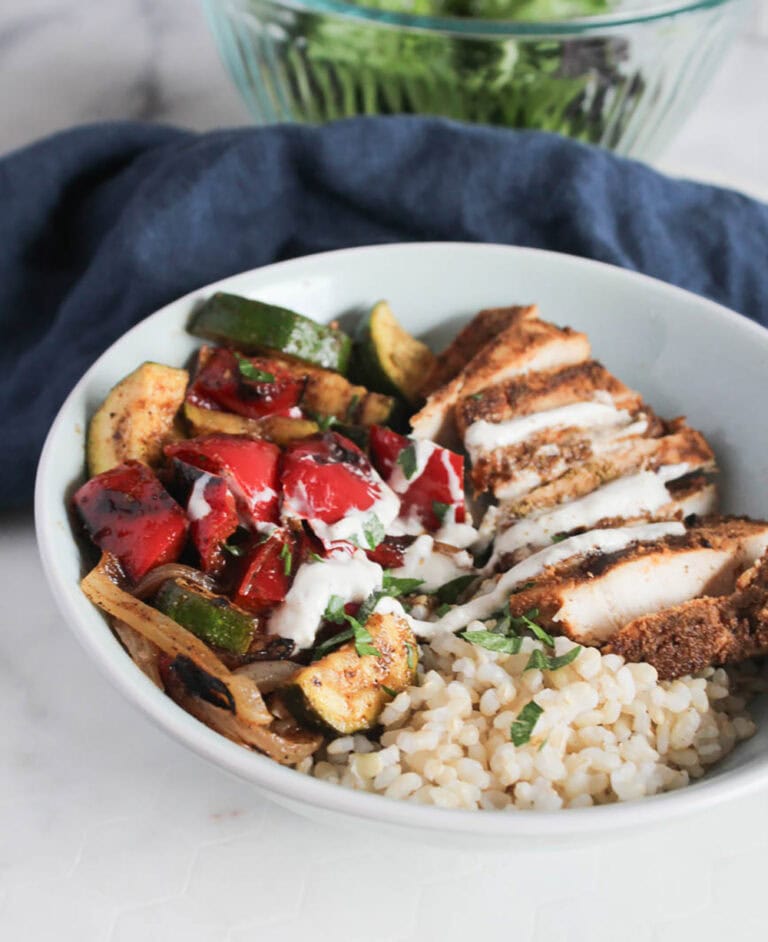 chicken shawarma bowl assembled: sliced cooked chicken breast, zucchini, peppers and rice drizzled with yogurt sauce