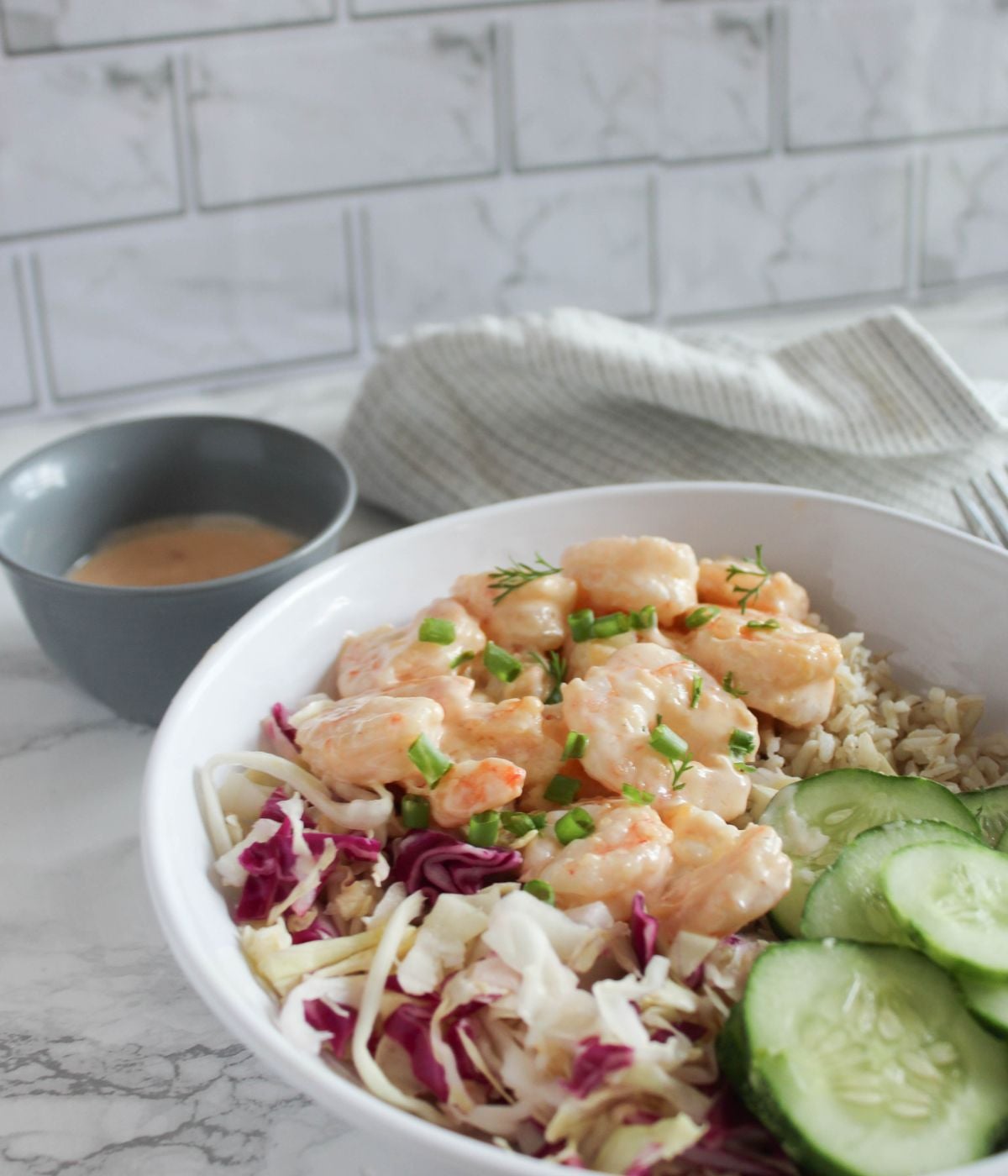 bang bang shrimp in a white bowl with cucumber slices, shredded cabbage and rice