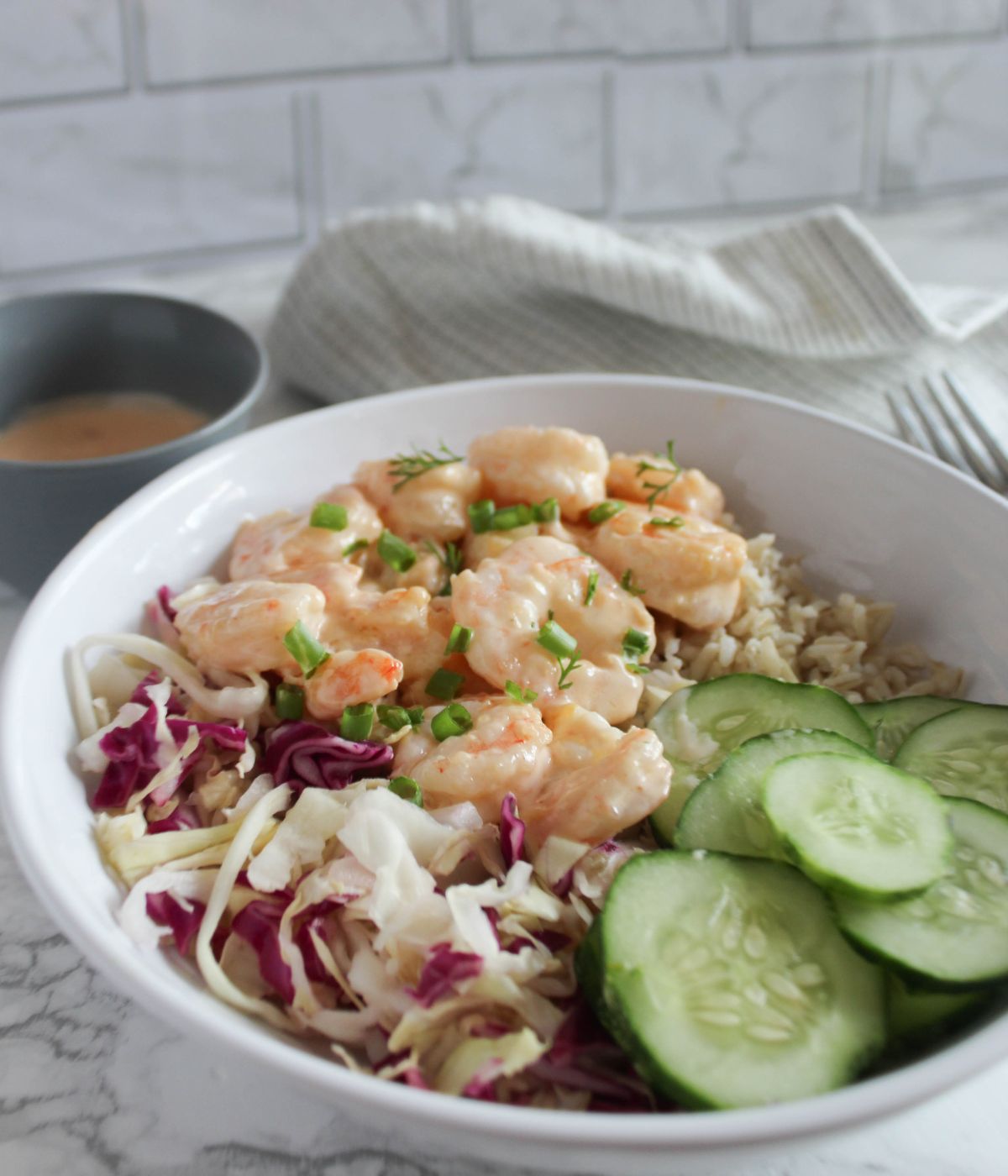 bang bang shrimp bowl - a white bowl filled with shrimp covered in bang bang bang sauce with shredded cabbage, sliced cucumbers and rice
